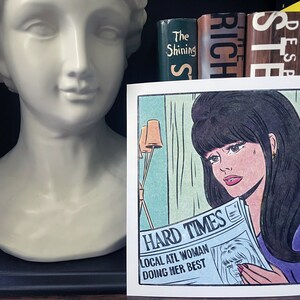 Puede incluir: Una ilustraci&oacute;n de estilo c&oacute;mic de una mujer leyendo un peri&oacute;dico con el titular "Hard Times: Local ATL Woman Doing Her Best". La mujer tiene el pelo oscuro y lleva una camisa morada. El peri&oacute;dico es azul y blanco.