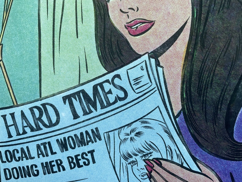 Puede incluir: Una mujer con el pelo largo y negro lee un peri&oacute;dico con el titular "HARD TIMES" y el subt&iacute;tulo "LOCAL ATL WOMAN DOING HER BEST".
