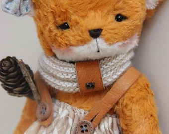 May include: A plush orange fox toy with black eyes and a white muzzle, wearing a light blue fabric bow on one ear, a cream-colored knit scarf with a brown leather tab, and a beige and white plaid skirt held up by brown leather suspender straps.