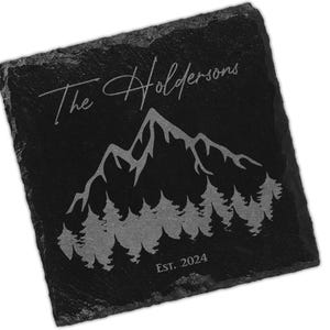 Può includere: Sottobicchiere in ardesia nera con un design di catena montuosa e alberi. Il testo "The Holdersons Est. 2024" è inciso in argento.