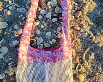 May include: Pink flamingo print tote bag with a white mesh bottom. The bag has two long straps and is perfect for carrying beach essentials.