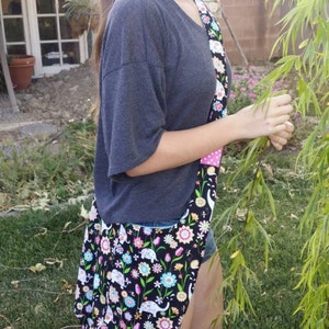 May include: A black tote bag with a colorful floral and elephant pattern. The bag has a wide strap with a pink polka dot design. The bag is worn over the shoulder.