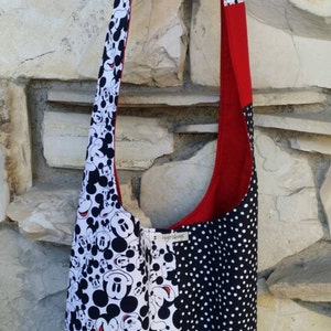 May include: A shoulder bag with a patchwork design. The bag features a black and white Mickey Mouse print, a black and white polka dot pattern, and a red accent. The strap is also red and patterned with Mickey Mouse.