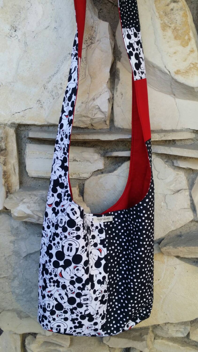 May include: A shoulder bag with a patchwork design. The bag features a black and white Mickey Mouse print, a black and white polka dot pattern, and a red accent. The strap is also red and patterned with Mickey Mouse.