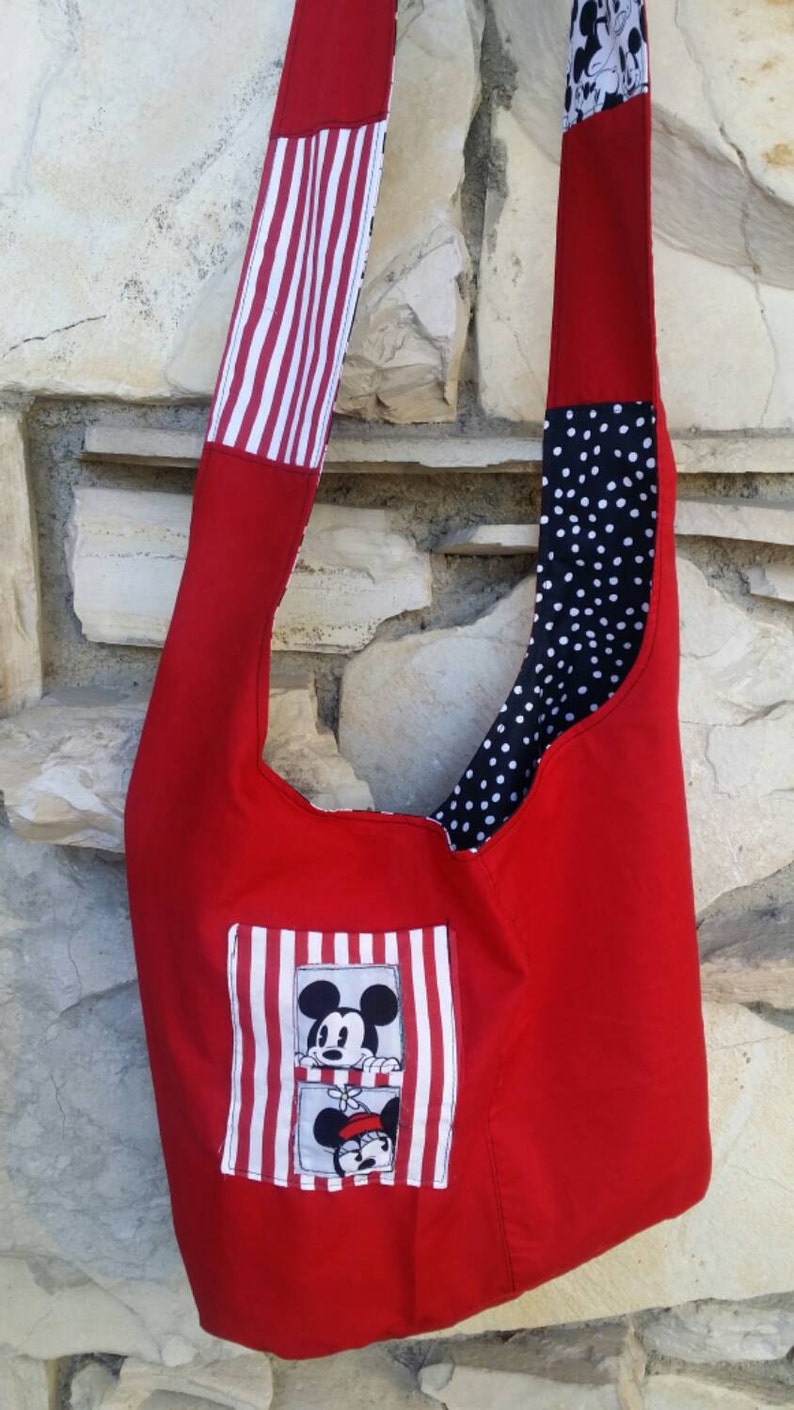 May include: A red shoulder bag with a Mickey Mouse and Minnie Mouse design. The bag features a red body, a white and red striped strap, and a black and white polka dot lining. The bag has a rectangular patch with Mickey and Minnie.