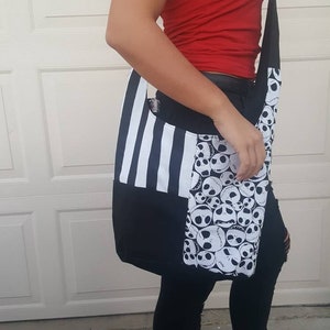 K&ouml;nnte beinhalten: Eine schwarz-wei&szlig; gestreifte und gemusterte Tragetasche mit einem schwarzen Riemen. Die Tasche hat ein Muster mit dem Gesicht von Jack Skellington aus dem Film Nightmare Before Christmas.