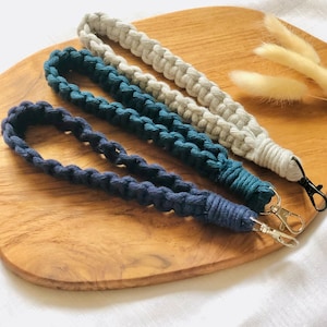 May include: Three braided keychains in different colors: white, teal, and navy blue. Each keychain has a silver metal clasp.