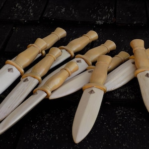 Puede incluir: Un grupo de ocho cuchillos de madera con un esquema de color marrón y beige. Cada cuchillo tiene un diseño en forma de diamante en la hoja.