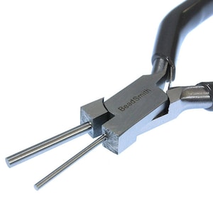 May include: Close-up of a silver beadsmith pliers with black handles. The pliers have two prongs for holding and shaping beads.
