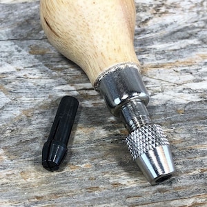 May include: A wooden handled rotary tool with a metal chuck and a black metal bit. The tool is on a wooden surface.