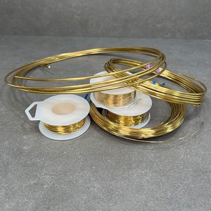May include: A close-up of several spools of gold-colored wire, some of which are unwound and lying on a gray surface.