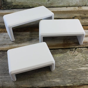 May include: Three white wooden risers, each with a rectangular shape and a slightly curved edge. The risers are arranged in a staggered formation, with the largest riser at the back and the smallest riser at the front.
