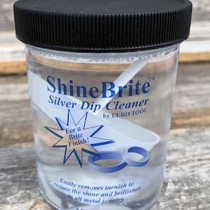 May include: A clear plastic bottle with a black lid containing a silver dip cleaner solution. The bottle is labeled "ShineBrite™ Silver Dip Cleaner by EURO TOOL" and has a starburst graphic with the text "For a Brite Finish!" The bottle also contains two silver rings and a white cleaning stick.