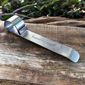 May include: A stainless steel metal tool with the text "BeadSmith EZ-BENDER" engraved on the side. The tool has a curved loop on one end and a flat, angled end. The tool is designed for bending metal.