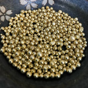 May include: A close-up of a bowl filled with small, shiny, gold-colored metal beads.
