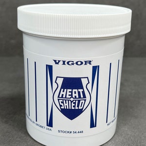 May include: White plastic jar with a blue and white logo that says "Vigor Heat Shield". The jar has a white lid and the text "STOCK# 54.448" printed on the bottom.