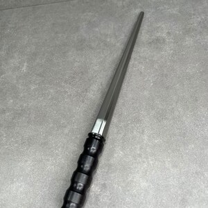 May include: A long, thin, silver-colored tool with a black, textured handle. The tool has a pointed tip and a slightly curved blade.