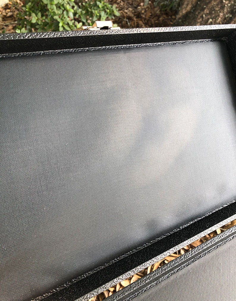 K&ouml;nnte beinhalten: Schwarze rechteckige Box mit weicher schwarzer Stoffauskleidung. Die Box hat einen silbernen Verschluss.