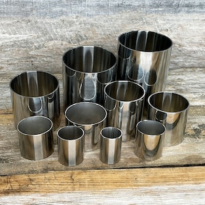 May include: A set of ten silver metal cake rings of varying sizes. The rings are arranged in a staggered pattern on a wooden surface.