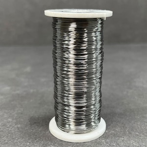 May include: A spool of silver-colored wire on a white plastic base. The wire is wound tightly around the spool.