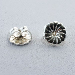 May include: Two silver earring backs, one is a standard butterfly back and the other is a round back with a decorative design.