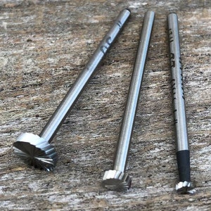 Puede incluir: Tres herramientas de metal plateado con puntas de diferentes formas. Las herramientas est&aacute;n sobre una superficie de madera.