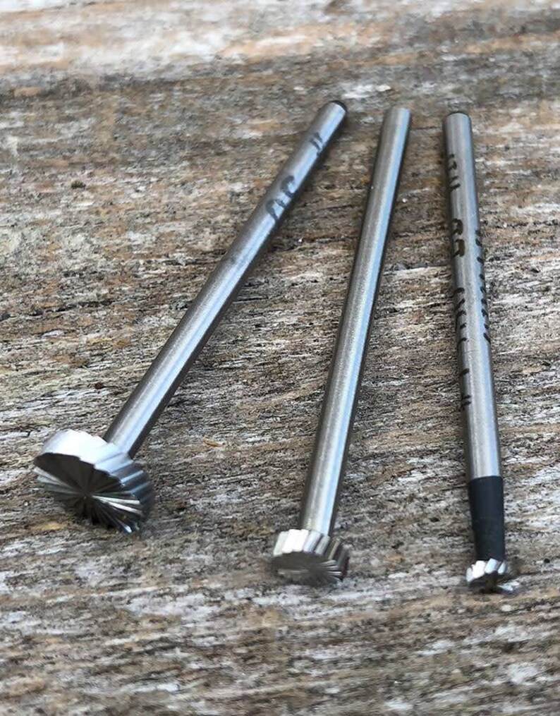 Puede incluir: Tres herramientas de metal plateado con puntas de diferentes formas. Las herramientas est&aacute;n sobre una superficie de madera.