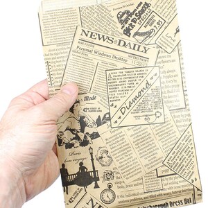 Pu&ograve; includere: Una busta di carta rettangolare con un design vintage di giornale. La busta &egrave; tenuta in mano e presenta titoli, articoli e illustrazioni in inchiostro nero su sfondo beige.