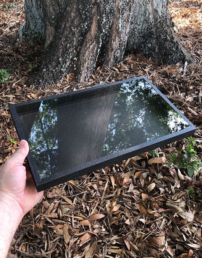 May include: A black rectangular display case with a clear glass top. The case is made of a textured material and has a sleek, modern design.