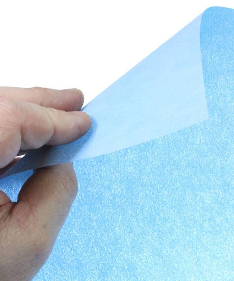 May include: A sheet of light blue glitter paper with a subtle sparkle. The paper is being held up by a hand, revealing the smooth, un-glittered side.