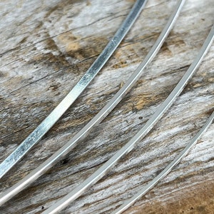 May include: Four silver metal strips, each with a slightly different width, are arranged in a fan shape on a wooden surface.