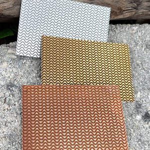 May include: Three rectangular metal sheets with a wavy pattern. The top sheet is silver, the middle is gold, and the bottom is copper-colored. The sheets are arranged in a stack, with the copper sheet at the bottom.