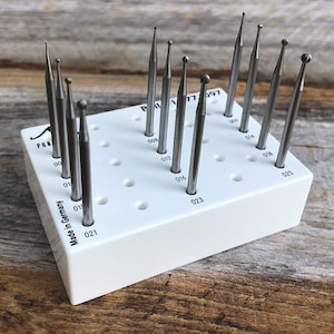 May include: A white plastic holder with a grid of holes, containing a set of 10 silver metal rotary tools. The tools are labeled with numbers from 00 to 025. The holder has the text "PAN 17997 Made in Germany" printed on it.