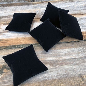 May include: Five black velvet ring display cushions on a wooden surface.