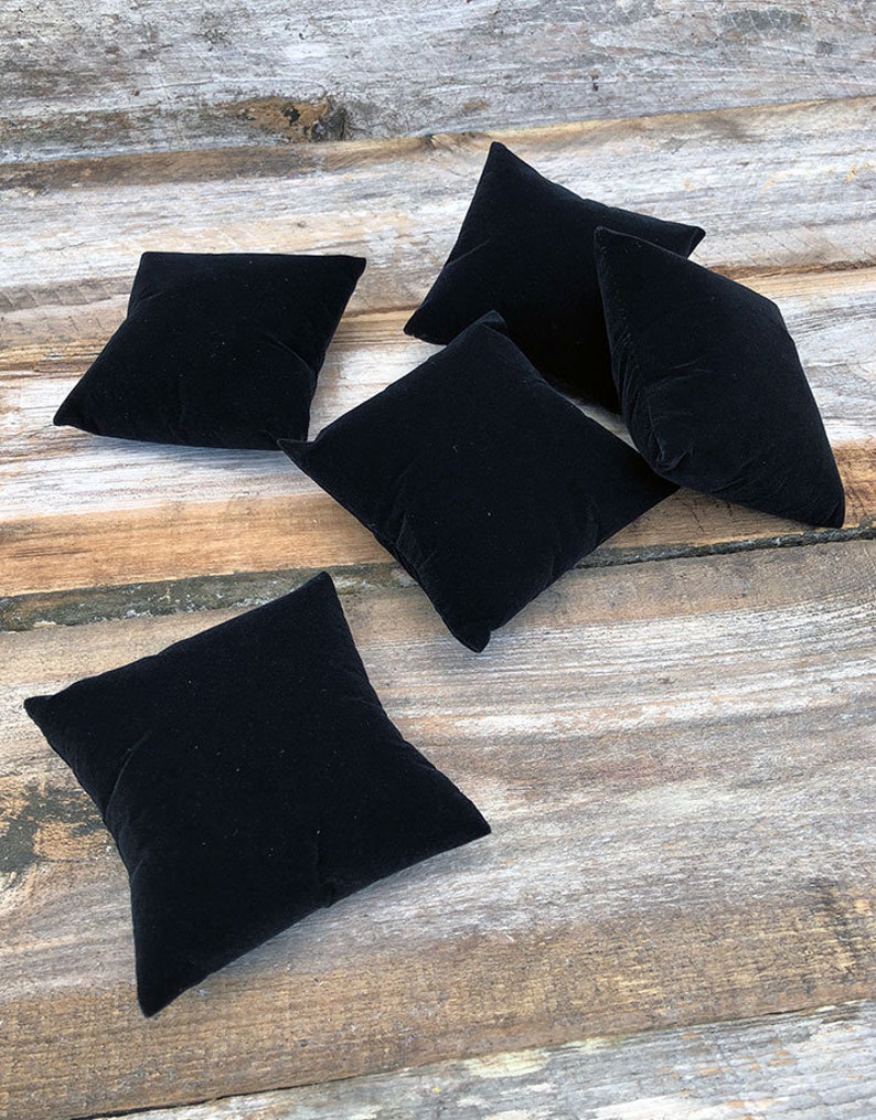 May include: Five black velvet ring display cushions on a wooden surface.