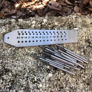 May include: A metal gauge with numbered holes from 7 to 20, and a set of 15 metal drill bits.