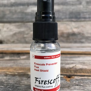 May include: A clear plastic bottle with a black spray nozzle. The bottle contains a clear liquid and has a white label with the text "Firescoff ceramic flux coating All-in-One" and "Firescale Preventer Flux Heat Shield".