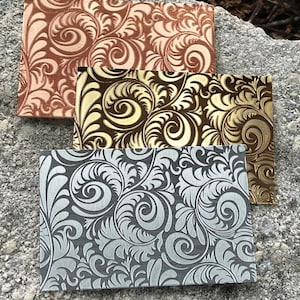 May include: Three decorative sheets of paper with a swirling floral pattern. The sheets are in shades of copper, gold, and silver.