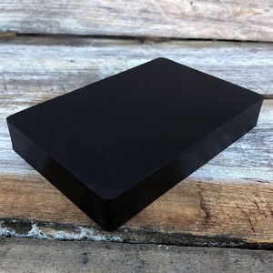 May include: A black rectangular block of soap on a wooden surface.