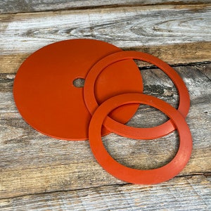 May include: Three orange silicone rings of different sizes. The largest ring is a flat disc with a small hole in the center. The other two rings are round and have a slightly raised edge.