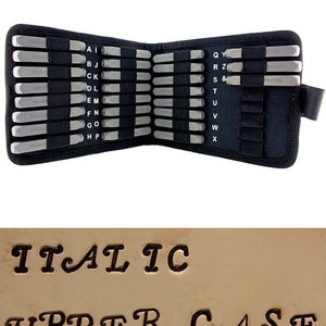 May include: A black leather case with a set of metal letter stamps for stamping metal. The case is open and the stamps are arranged in alphabetical order. The stamps are labeled with the letters of the alphabet. The case is labeled "BEADS" on the side. The image also shows a sample of the stamped letters in italic uppercase.