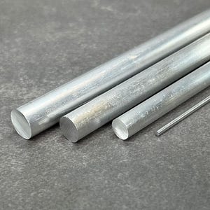 May include: Four silver metal rods of varying diameters, arranged in a row on a gray surface.