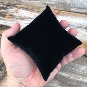 May include: A small, black velvet cushion, ideal for displaying jewellery or other small items.