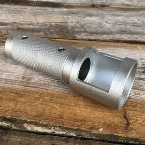 May include: A silver-colored metal tool with a textured grip and a rectangular opening. The tool has a cylindrical body with two small holes near the grip. The tool is designed for a specific purpose.