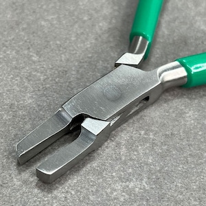 May include: Close-up of a pair of green handled pliers with a silver metal head. The pliers have a flat jaw with a rounded edge.