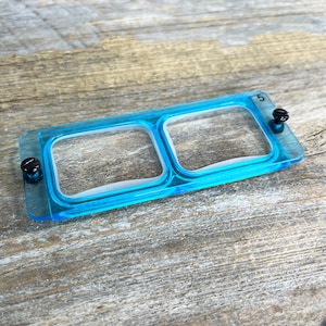 May include: A blue plastic tray with two clear square compartments. The tray has two black screws on each side.