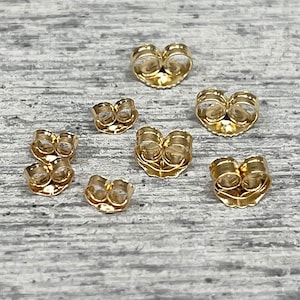 May include: A set of seven gold-toned earring backs. The backs are made of metal and have a butterfly closure.