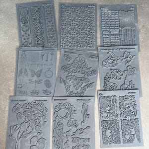 May include: Set of ten black and gray rubber stamps with various designs, including floral patterns, geometric shapes, and text. The stamps are arranged in two rows of five. The text on the stamps includes "World Tour Craft" and "Chalk It Up".