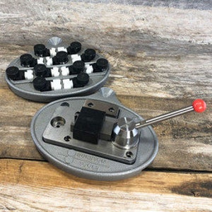 May include: A metal jewelry making tool with a lever and a base with a grid of black and white squares. The tool is designed for making jewelry.