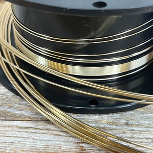 May include: A spool of gold-colored wire wound around a black plastic spool. The wire is thin and shiny.